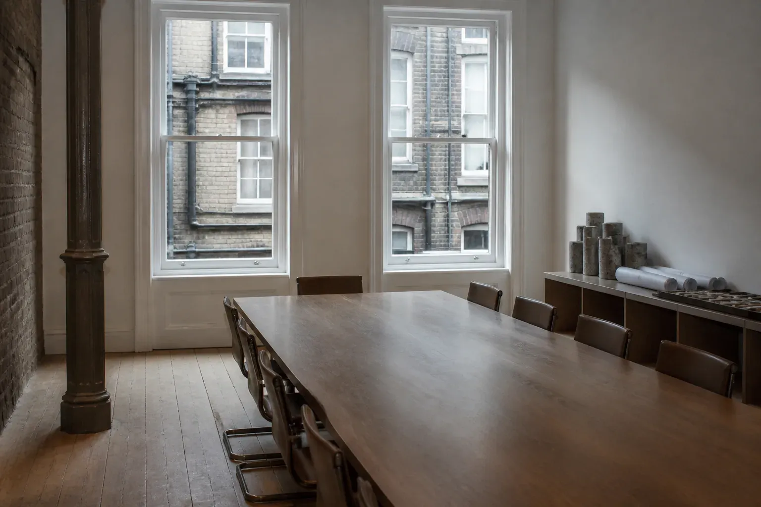A plain meeting room in a converted brick building, with a long oak table, tall sash windows and drill core samples on a side console.